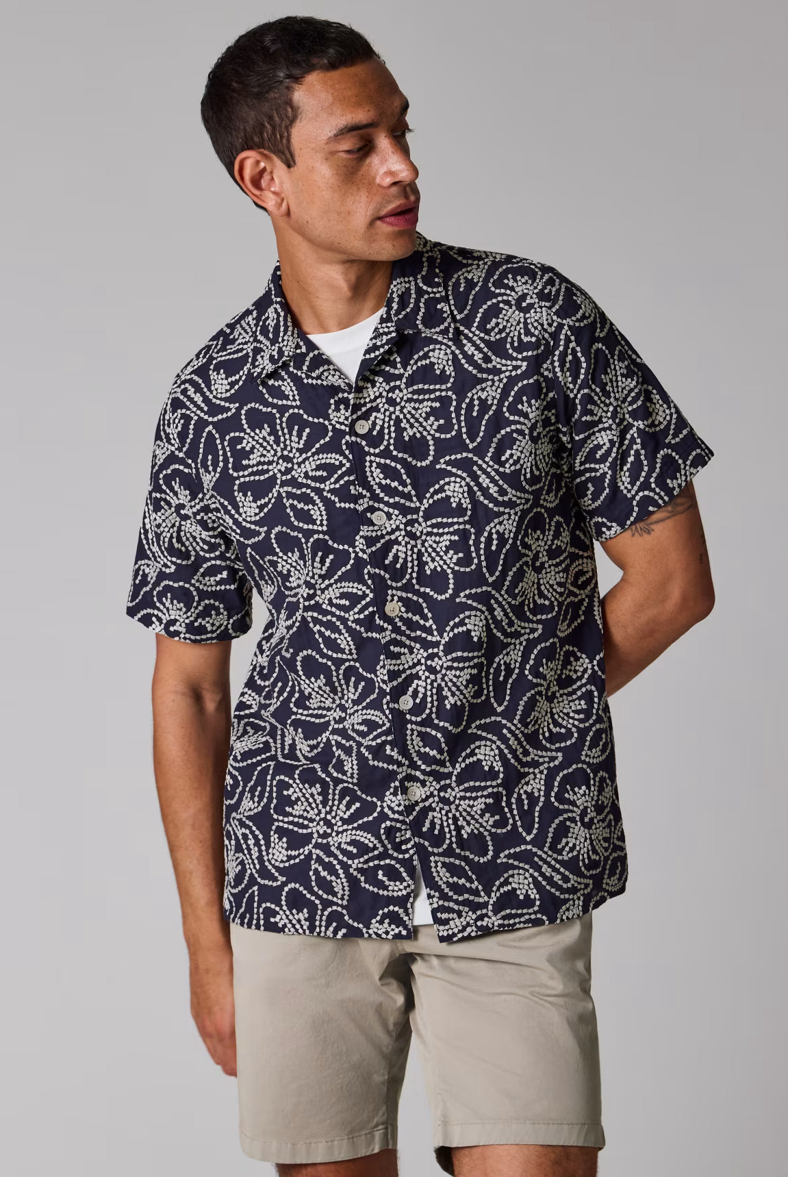 Man wearing a navy patterned shirt and beige shorts on a gray background