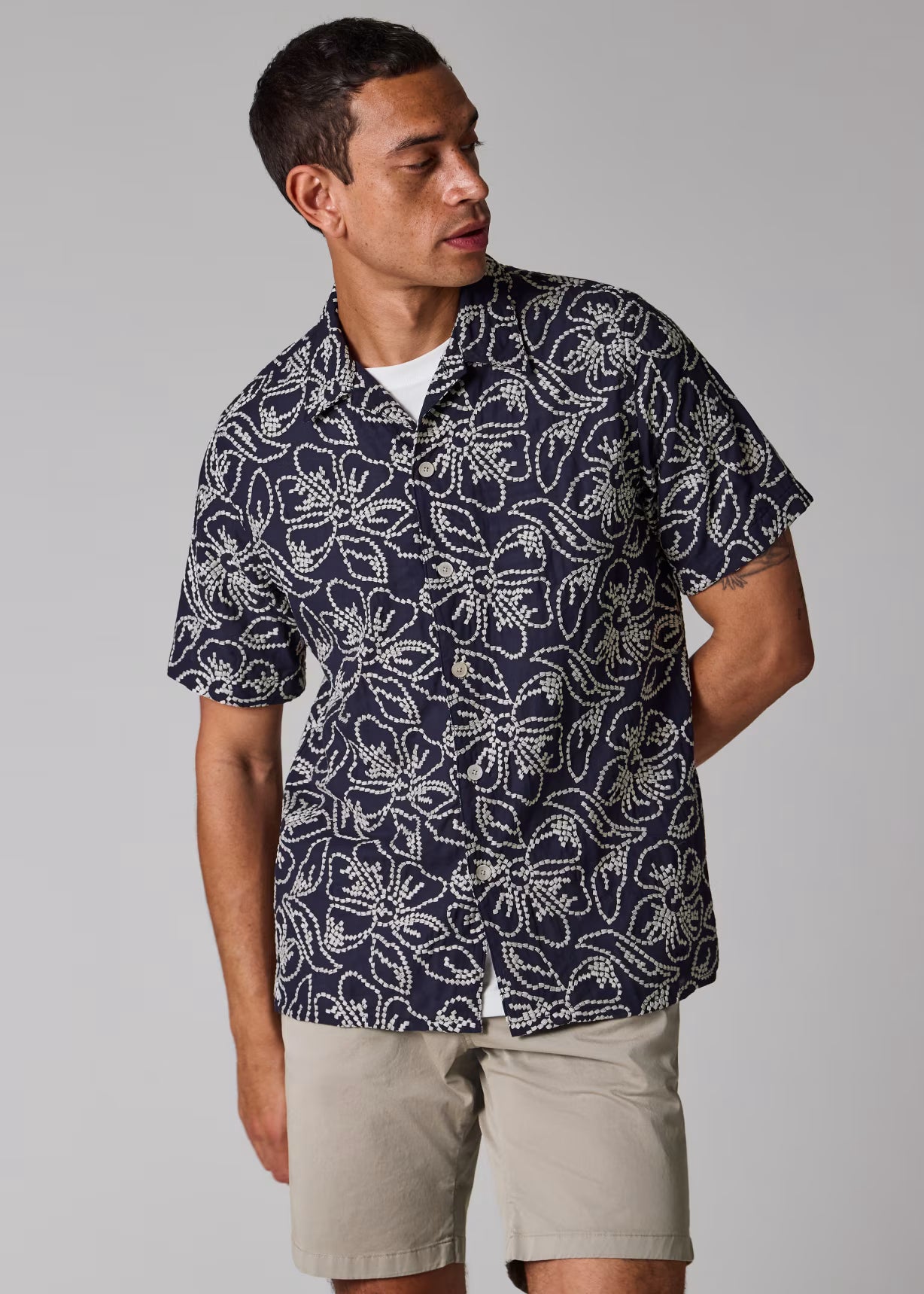 Man wearing a navy patterned shirt and beige shorts on a gray background