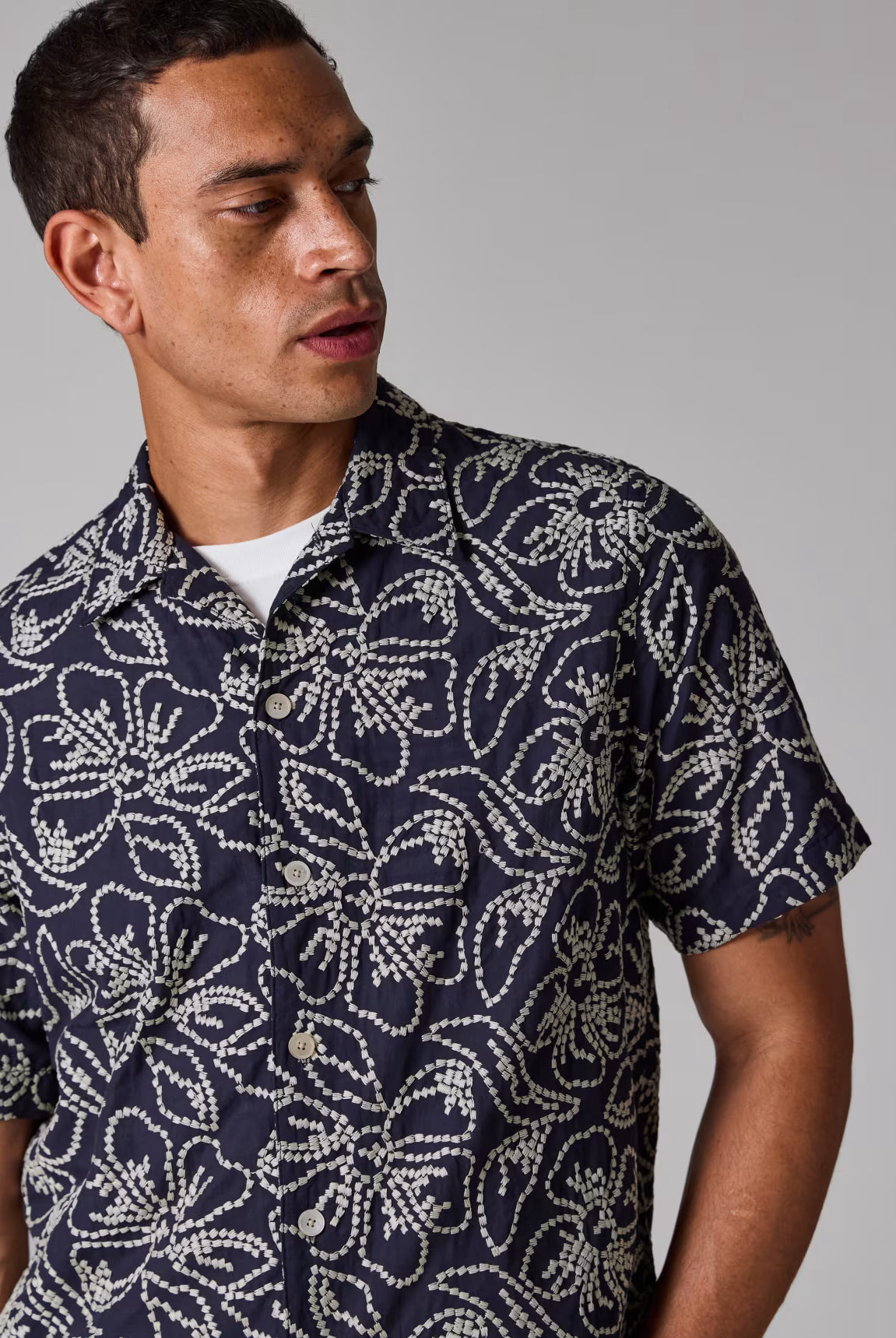 Man wearing a navy patterned shirt against a gray background