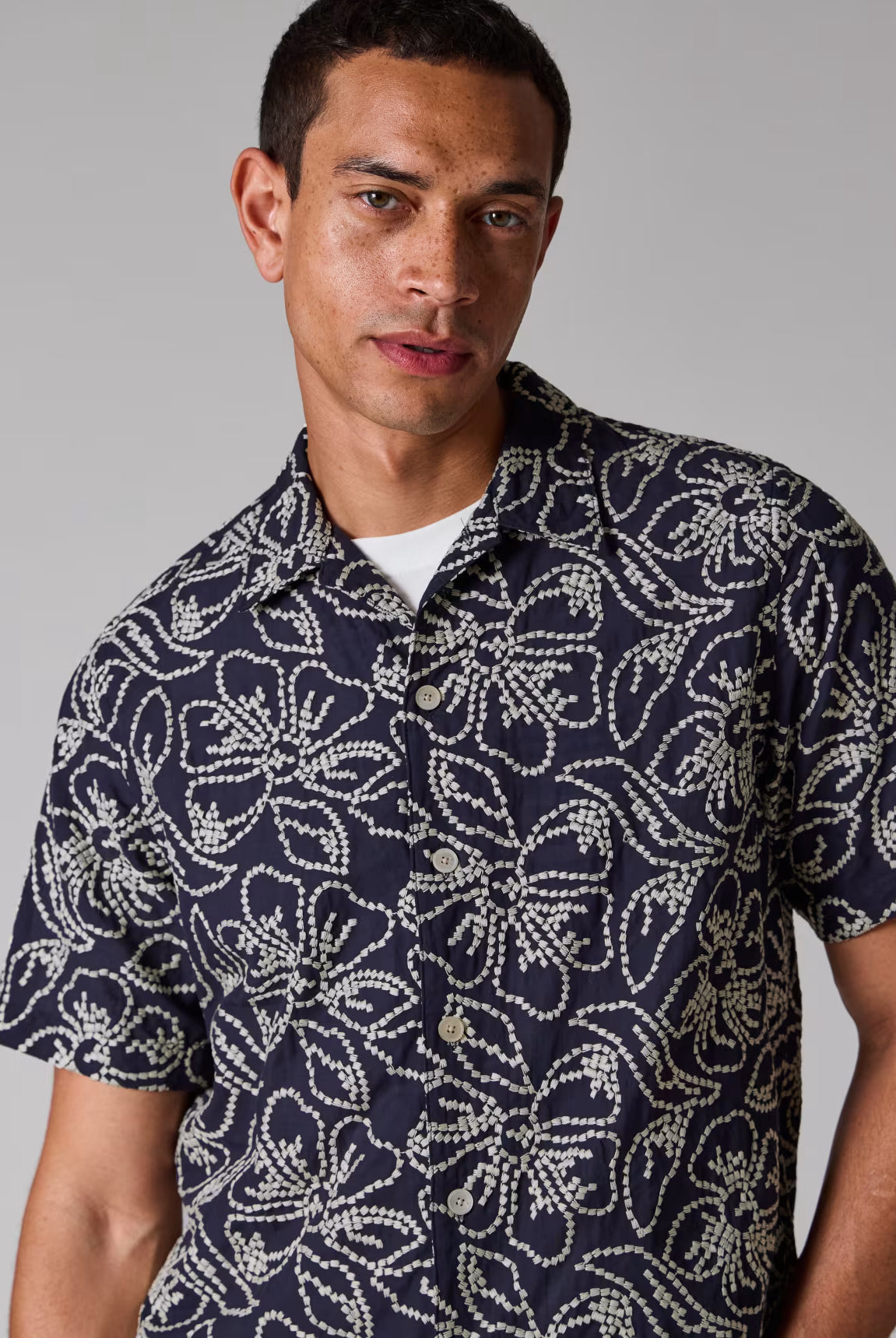 Man wearing a navy patterned shirt against a gray background