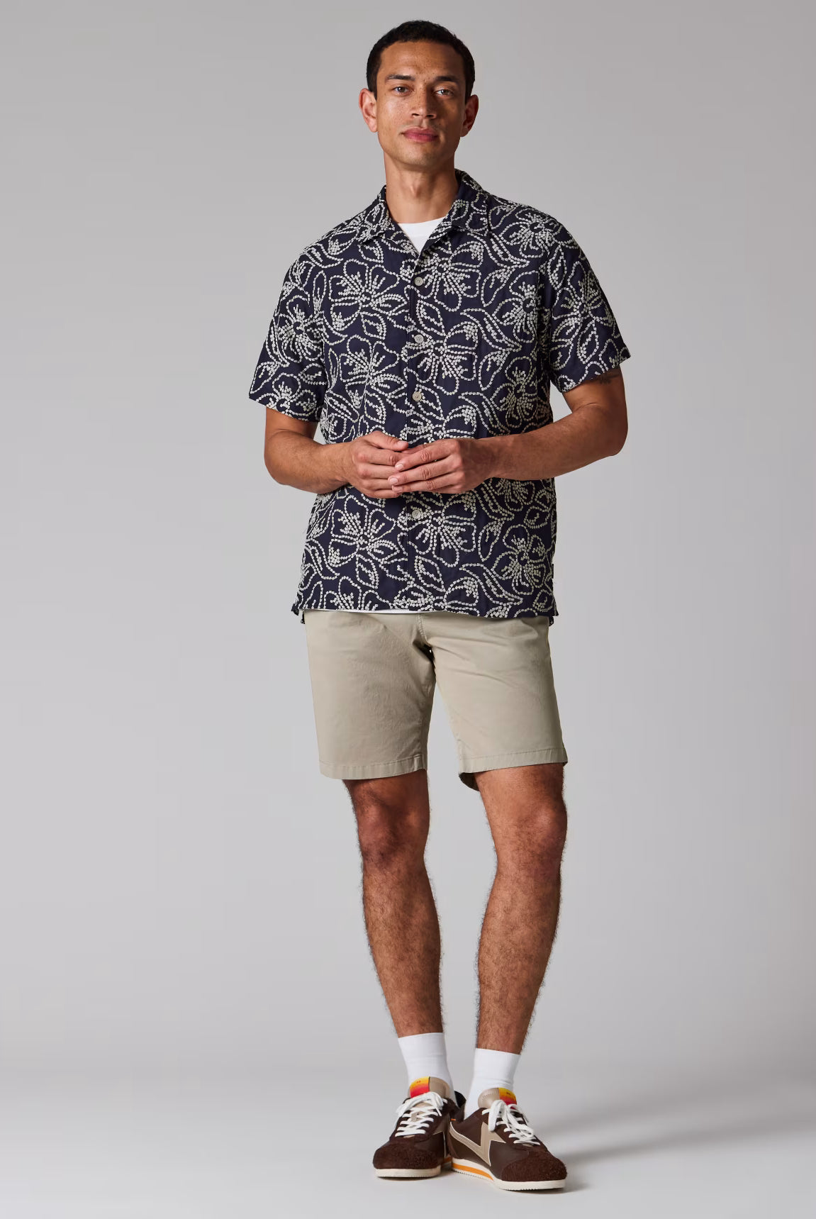 Man wearing a patterned shirt and beige shorts on a plain background