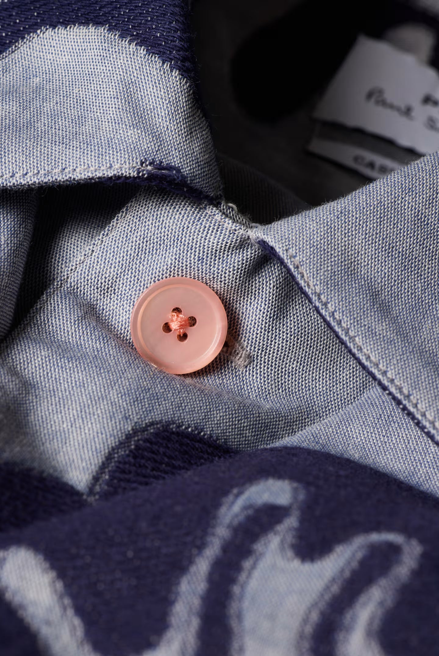 Close-up of a button on a denim shirt with a brand tag in the background.