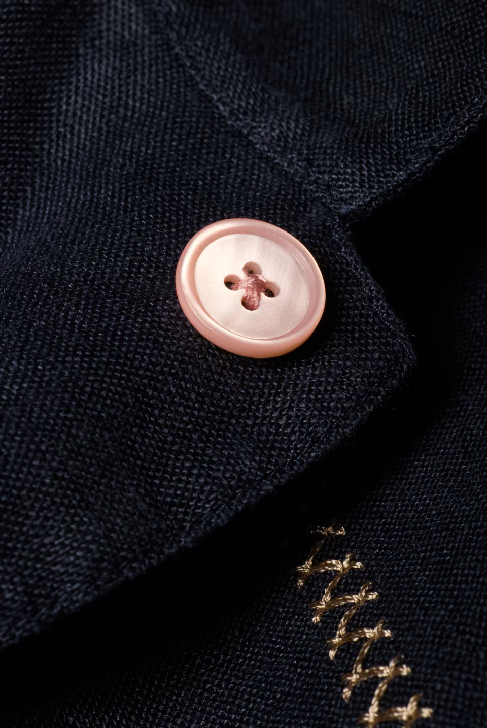 Close-up of a button on a dark fabric with gold embroidery.