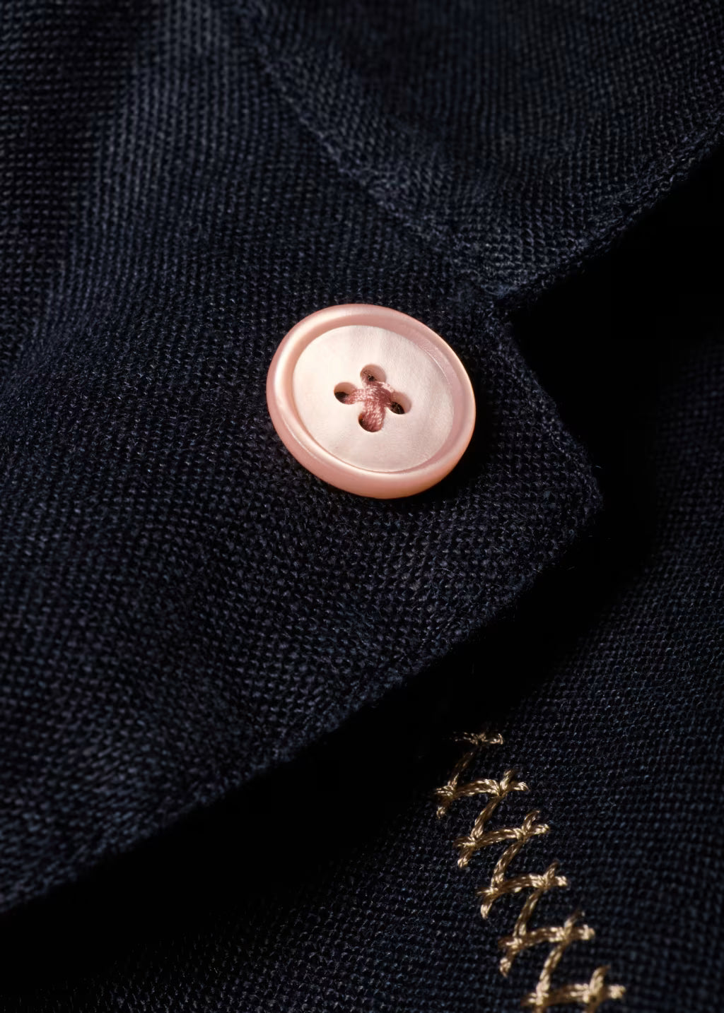 Close-up of a button on a dark fabric with gold embroidery.