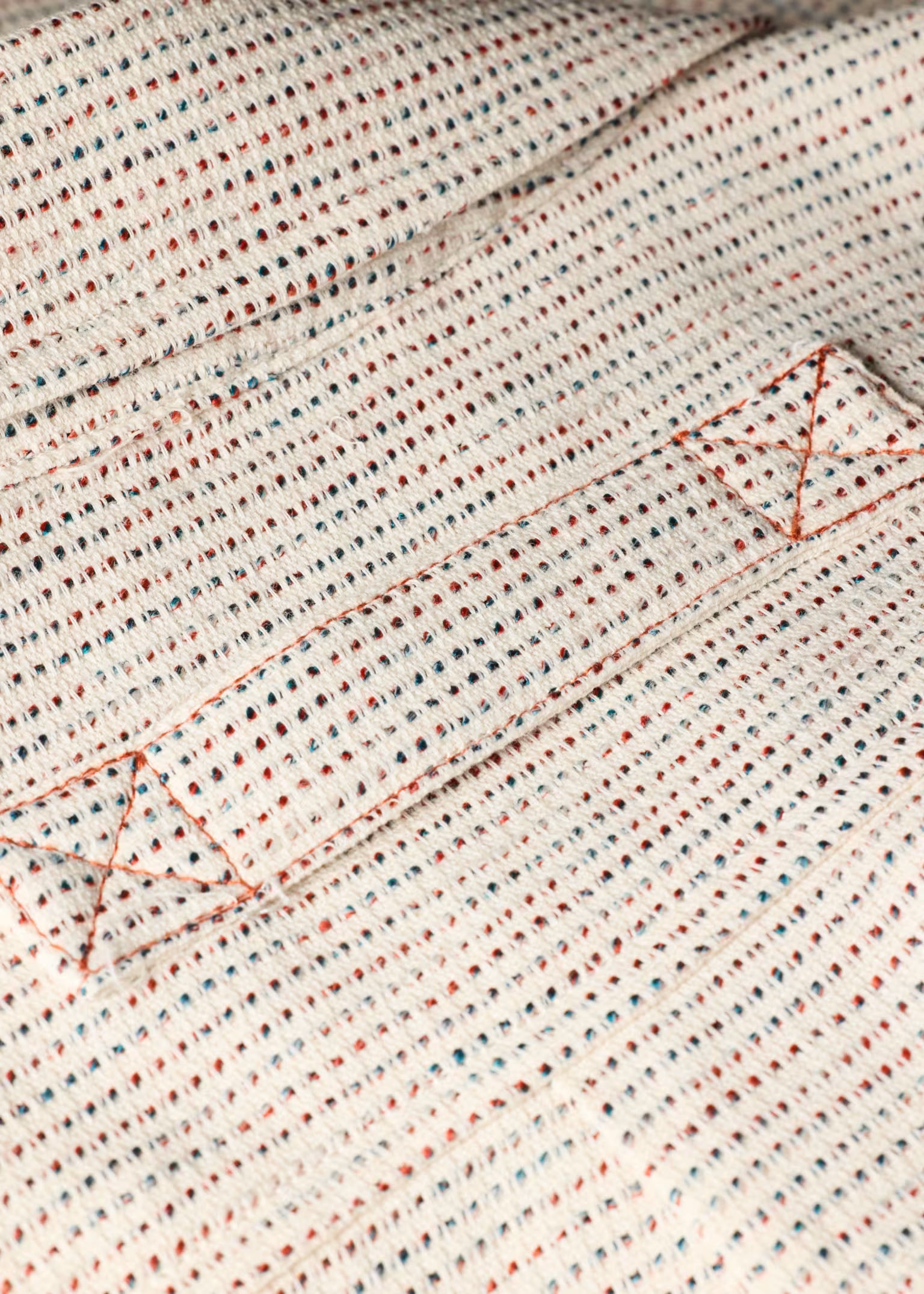 Close-up of a textured fabric with red and blue patterns on a beige background
