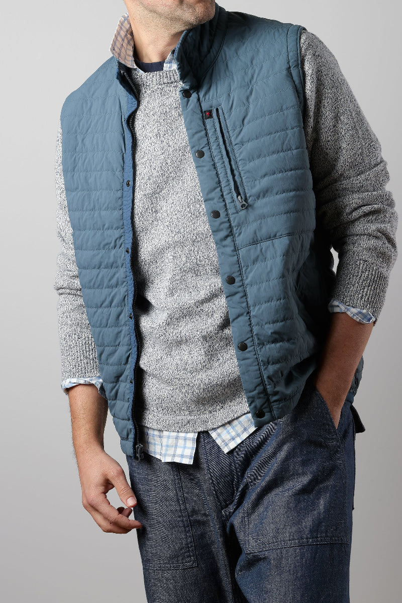 Person wearing a blue quilted vest over a gray sweater with a neutral background