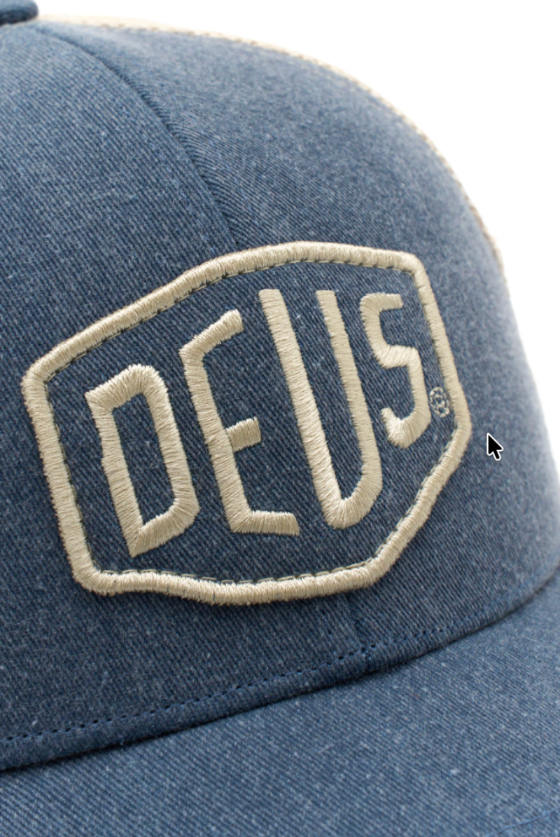 Blue denim cap with 'DEUS' logo on a white background
