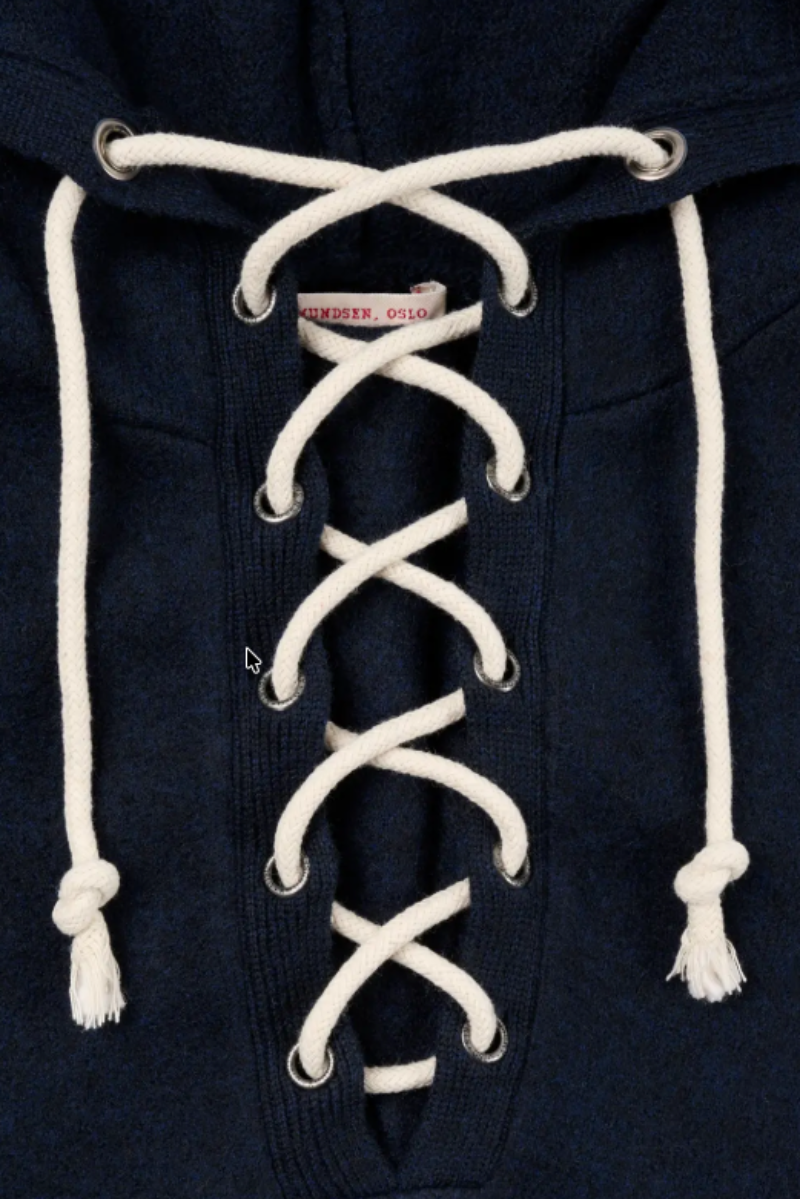Close-up of a navy blue hooded sweatshirt with white laces threaded down the front and white drawstrings at the hood.
