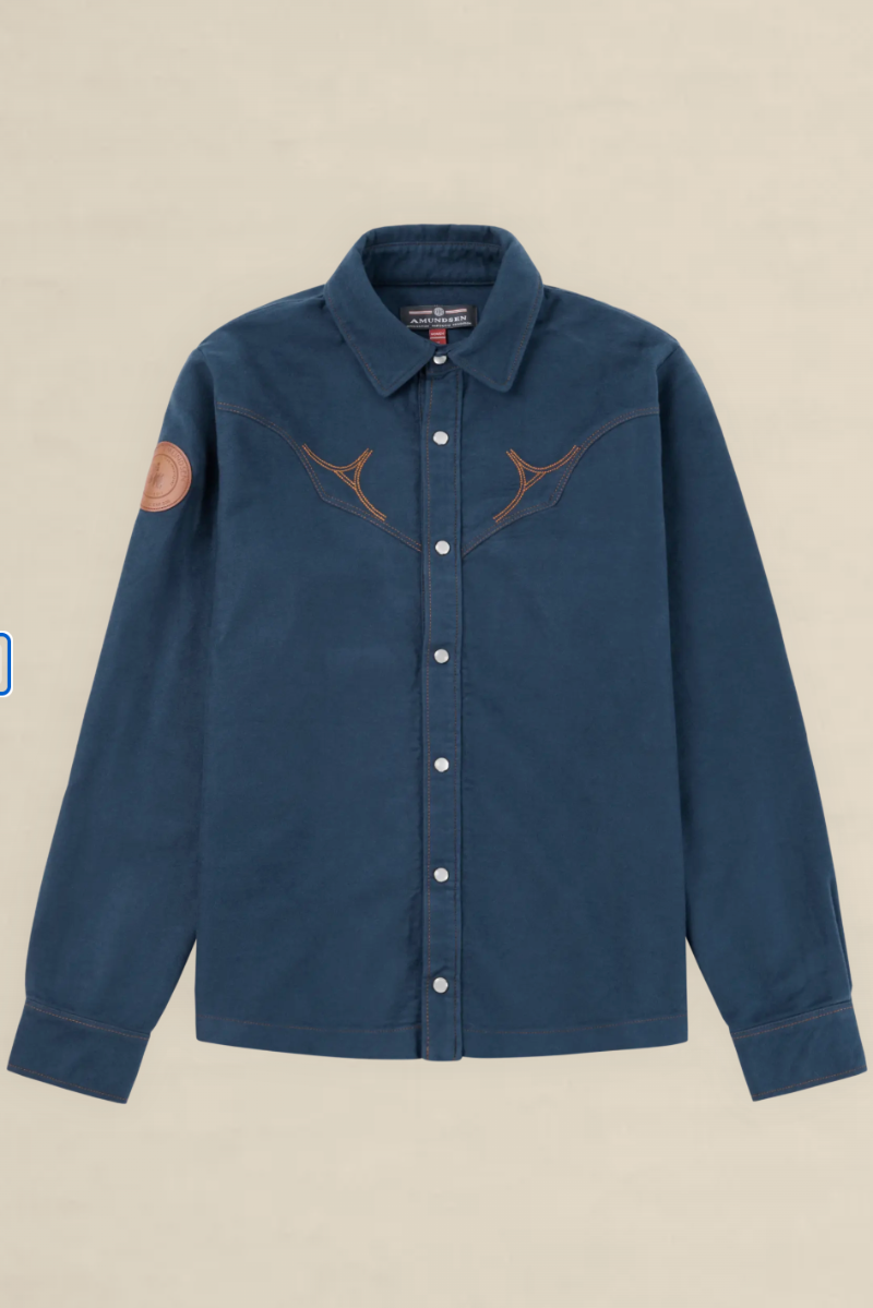 A dark blue denim western-style shirt jacket with brown embroidered antlers across the chest, a brown circular patch on the right sleeve, and white buttons, shown against a light beige background.