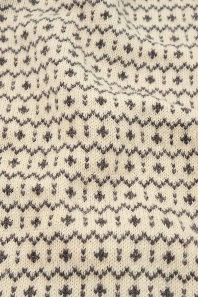 Close-up of a cream-colored knit fabric with a dark gray Fair Isle pattern of small geometric motifs.