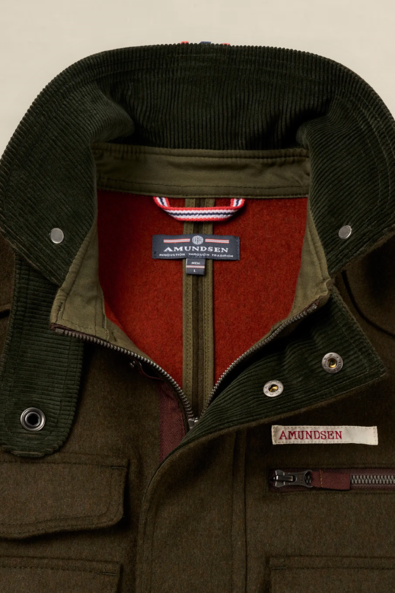 Close-up of an Amundsen jacket showing the interior collar, olive green corduroy lapels, red fleece lining, and a sewn-on brand label on the chest pocket.