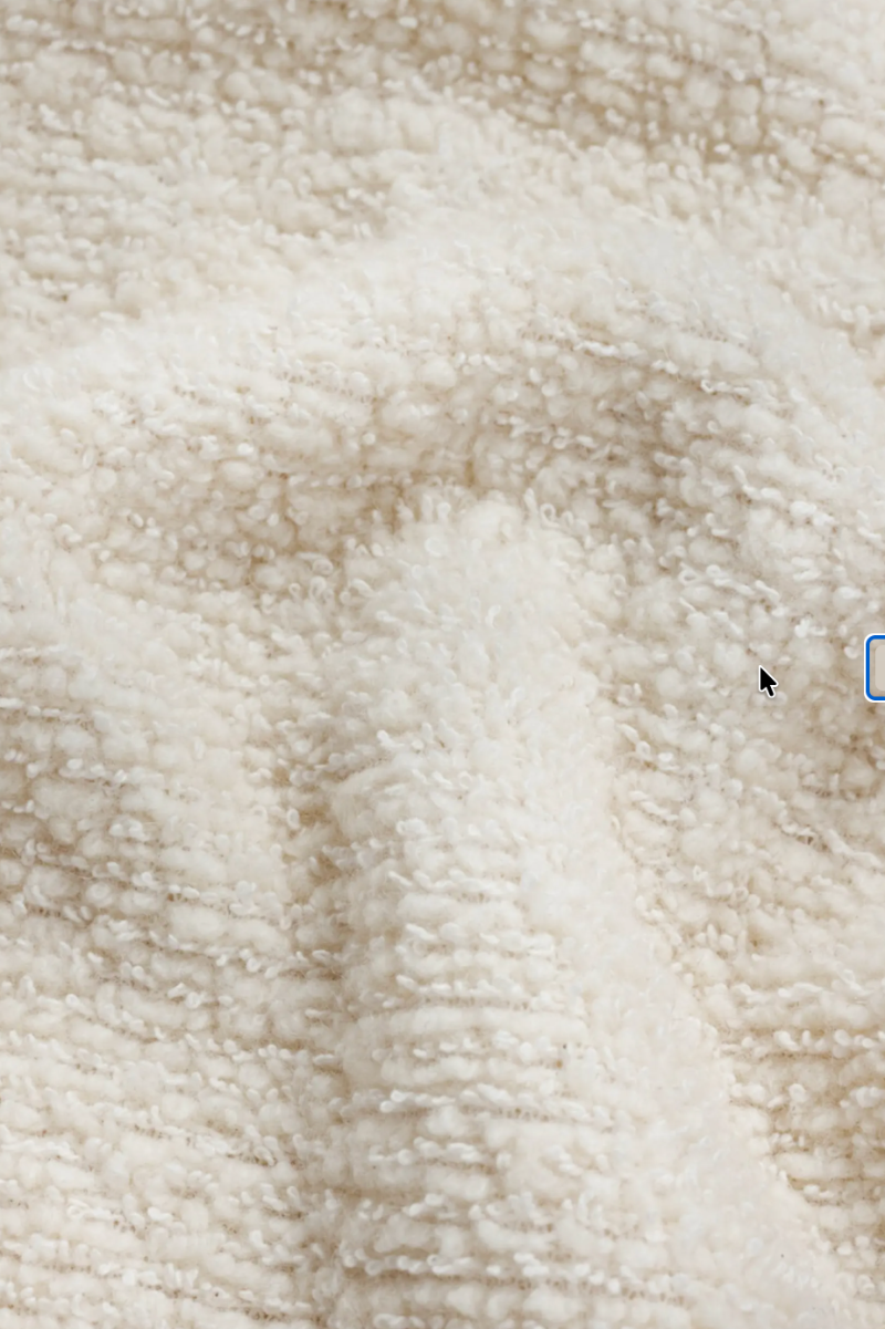 Close-up of a soft, plush fleece or sherpa fabric in a warm off-white or cream color, showing the textured loop pile and gentle folds.