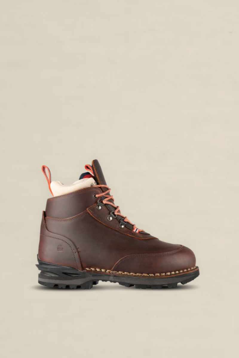 A single dark brown leather hiking boot with orange laces and a cream-colored collar lining, shown in a side profile against a solid light beige background.