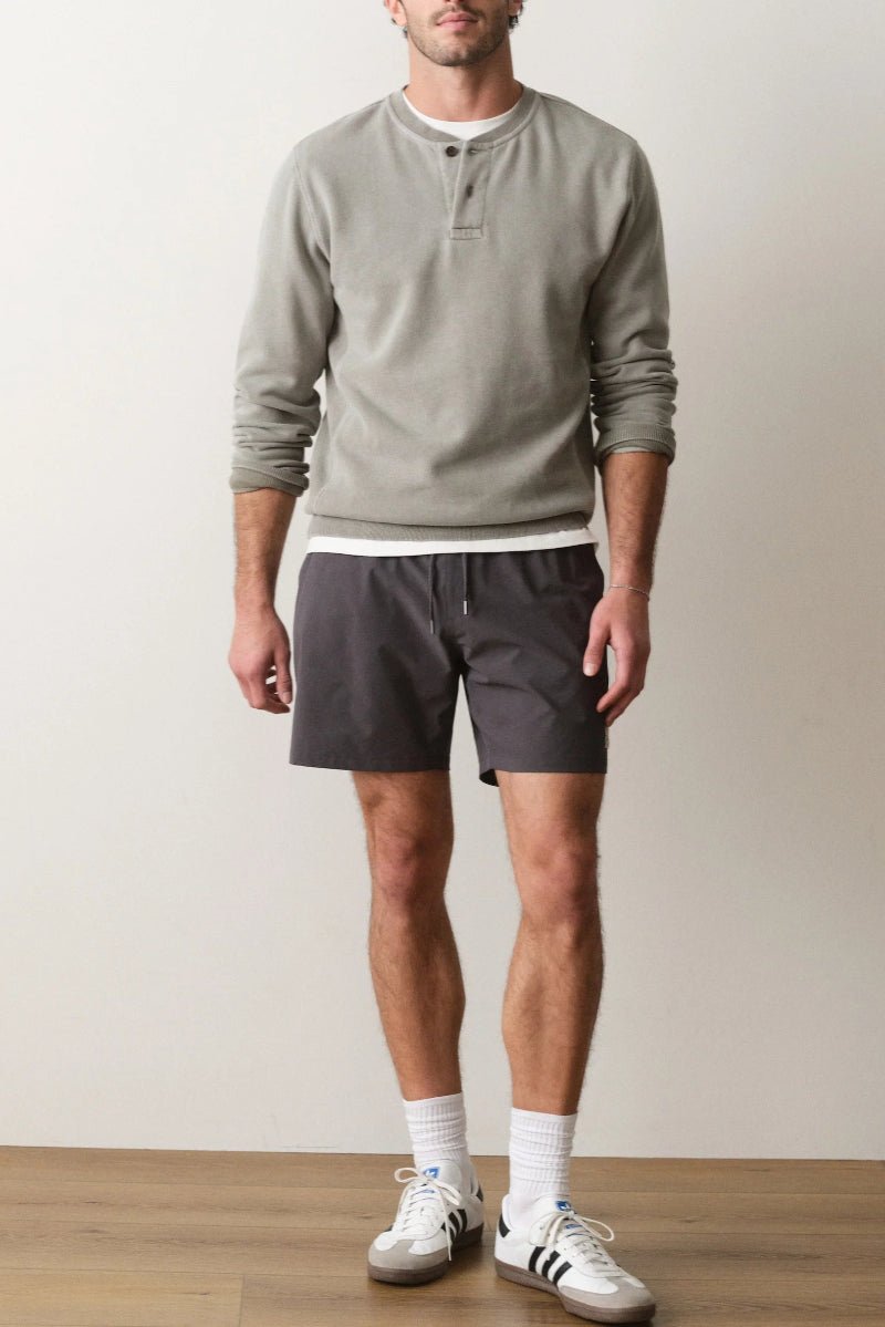 Man wearing a light gray sweatshirt, dark shorts, white socks, and white sneakers on a plain background