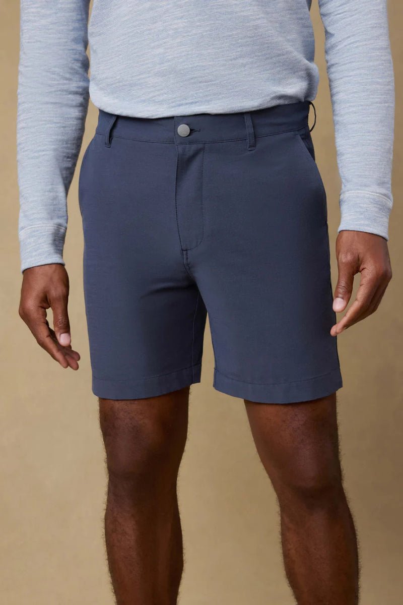 Person wearing navy shorts and a light gray long-sleeve shirt against a beige background