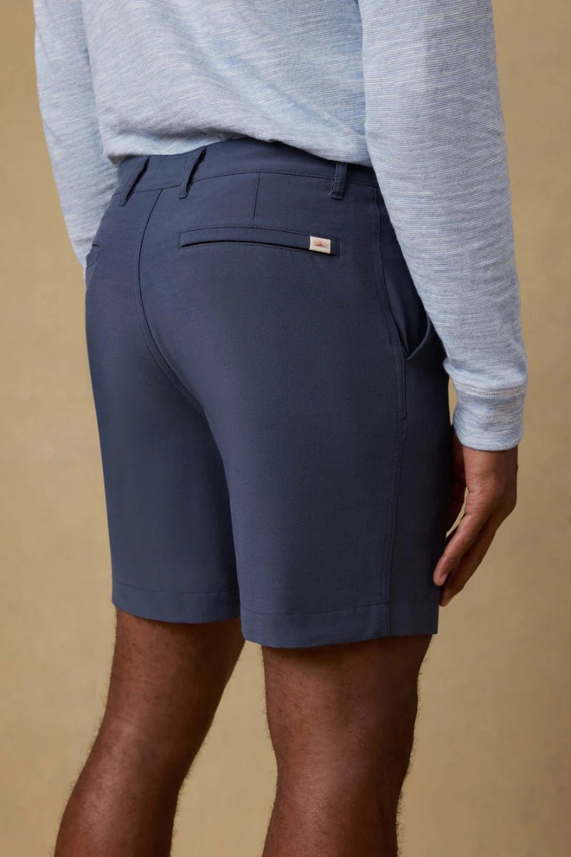 Person wearing navy shorts and a light gray long-sleeve shirt against a beige background