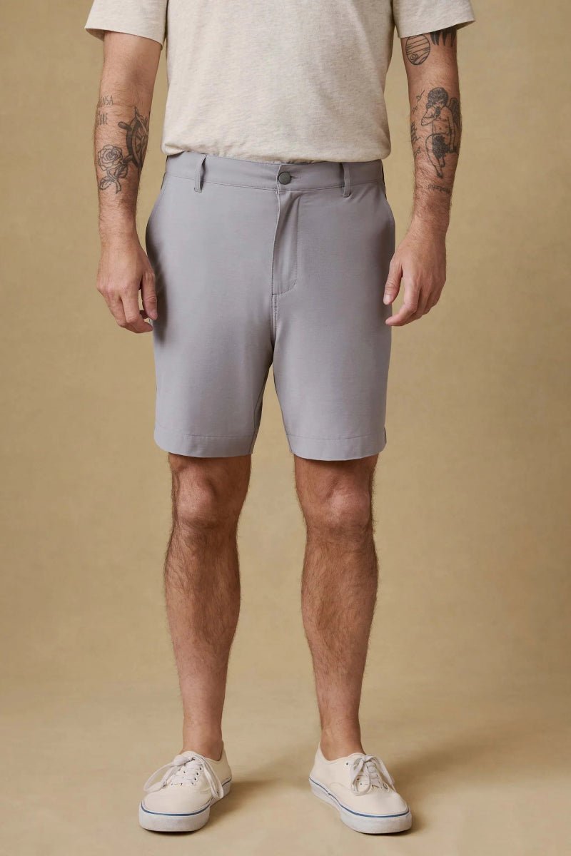 Person wearing gray shorts and white sneakers on a beige background