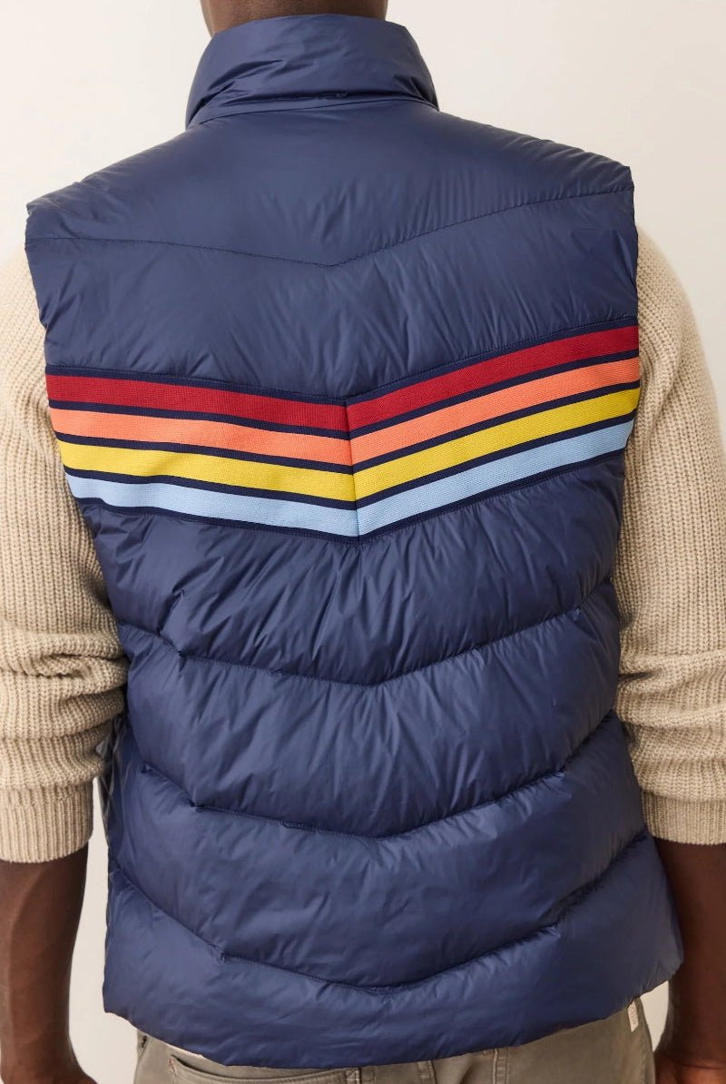 Blue puffer vest with colorful stripes worn by a person on a plain background