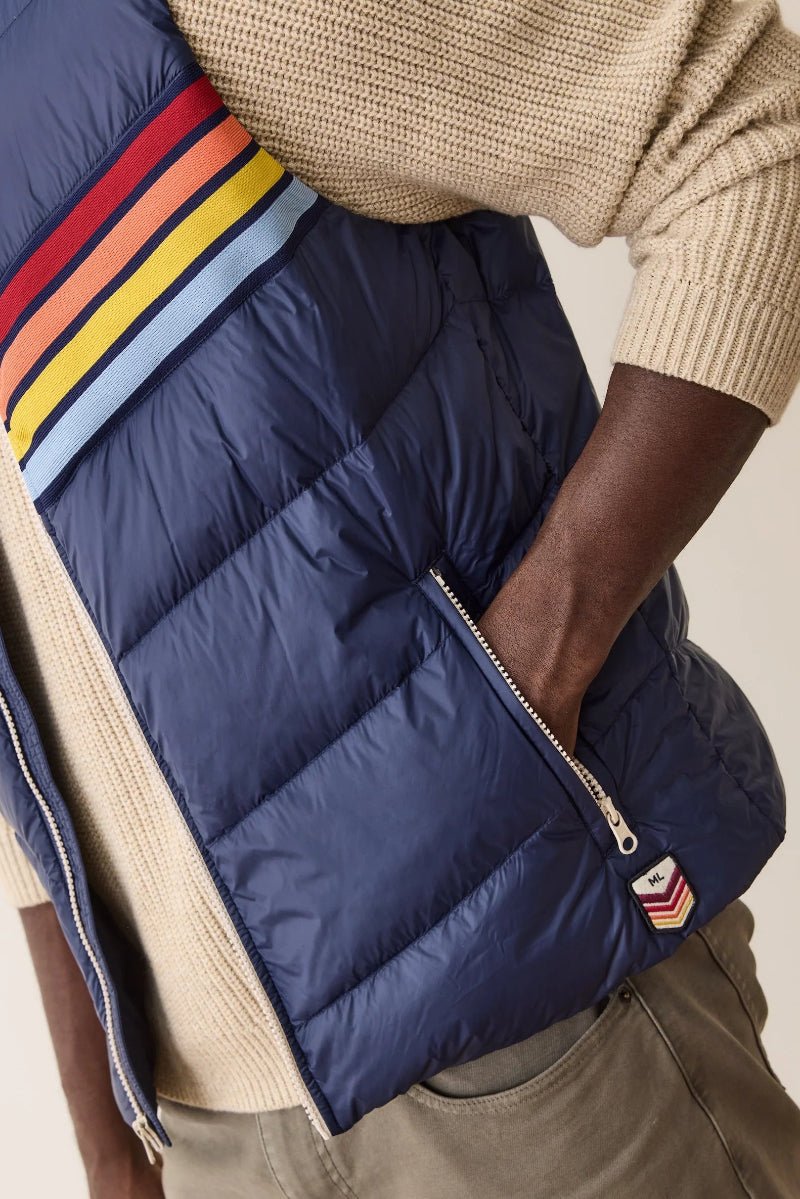 Person wearing a navy puffer vest with colorful stripes on a neutral background