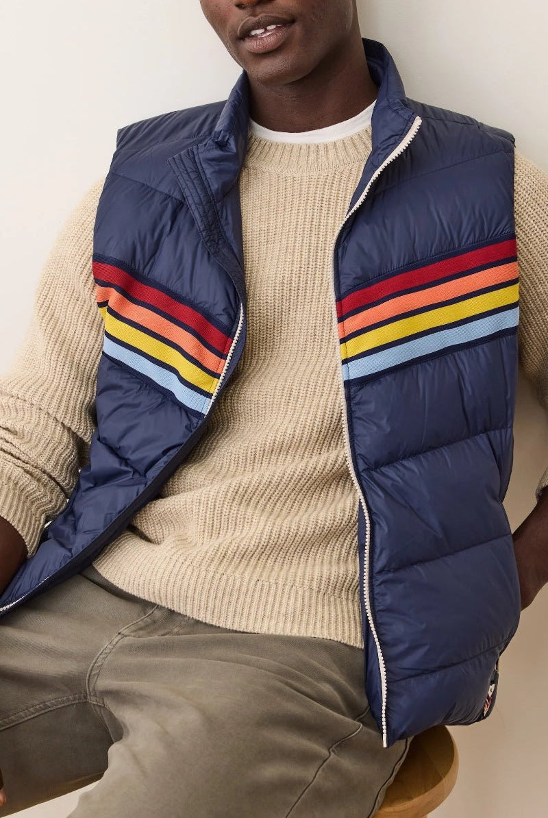 Person wearing a blue puffer vest with colorful stripes over a beige sweater.