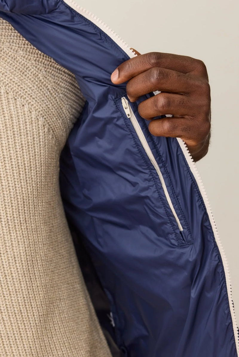 Hand zipping a navy blue jacket over a beige garment on a neutral background