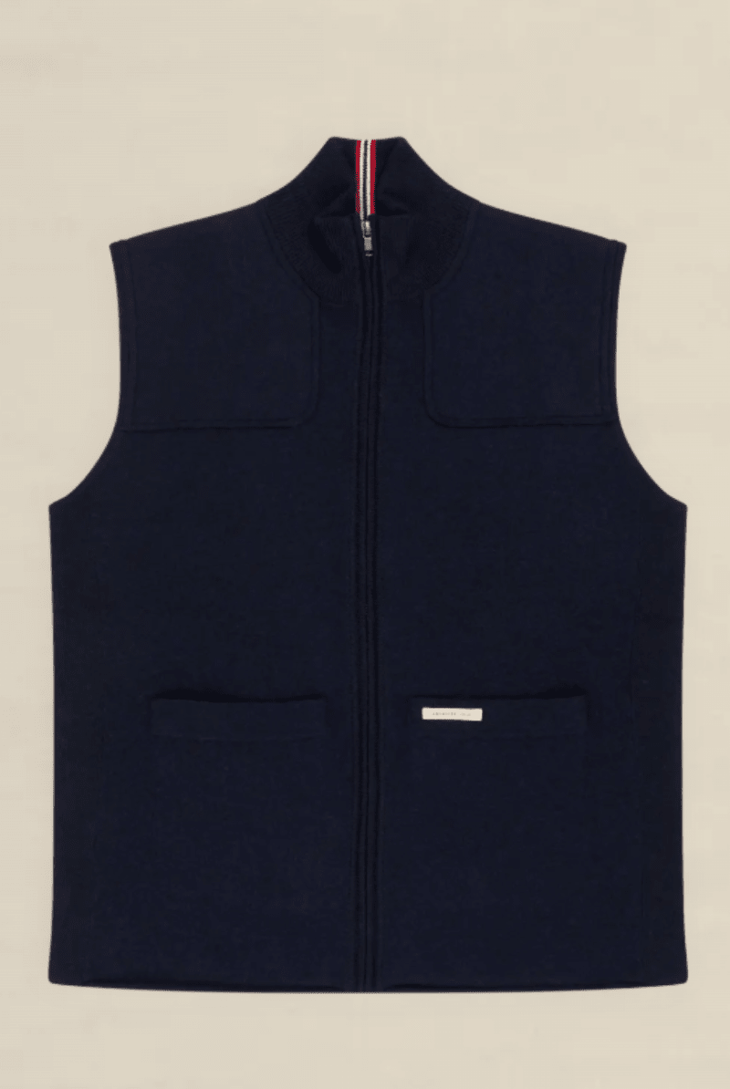 A navy blue zip-up fleece vest with a mock neck, two front patch pockets, and a small white brand label on the lower front pocket, shown flat against a light beige background.