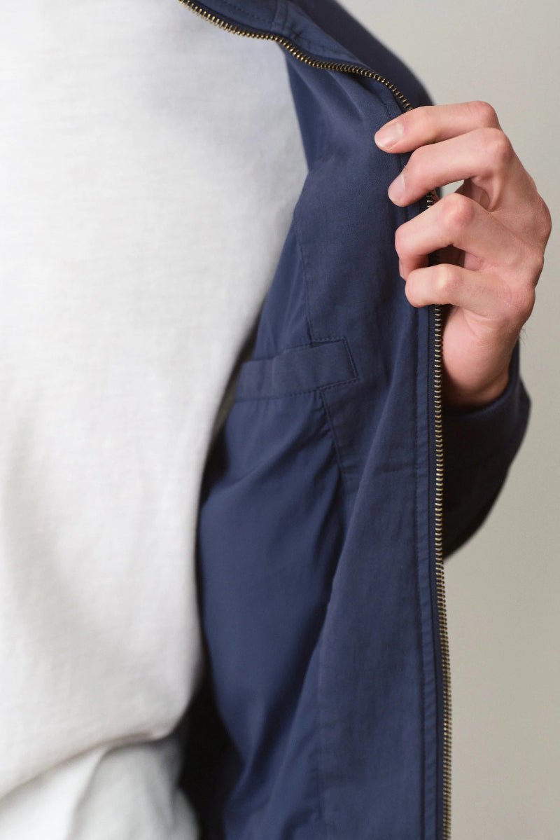 Person wearing a navy jacket with a white shirt underneath, holding the zipper.
