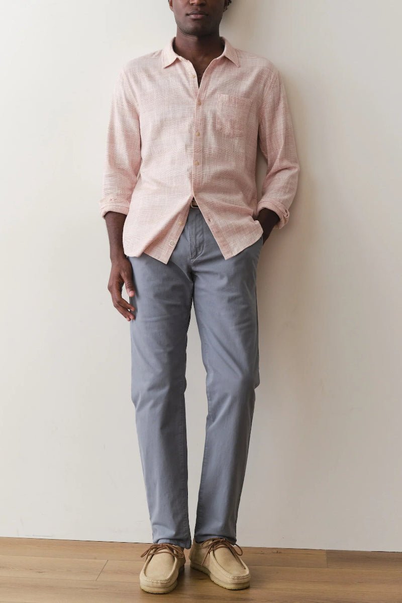 Person wearing a light pink shirt and gray pants standing against a white wall.