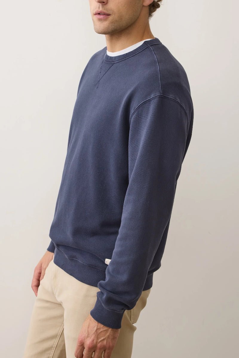 Man wearing a navy blue sweatshirt and beige pants against a plain background