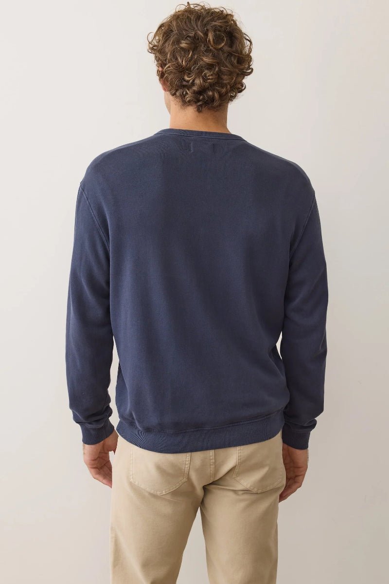 Person wearing a navy blue sweater and beige pants against a plain background