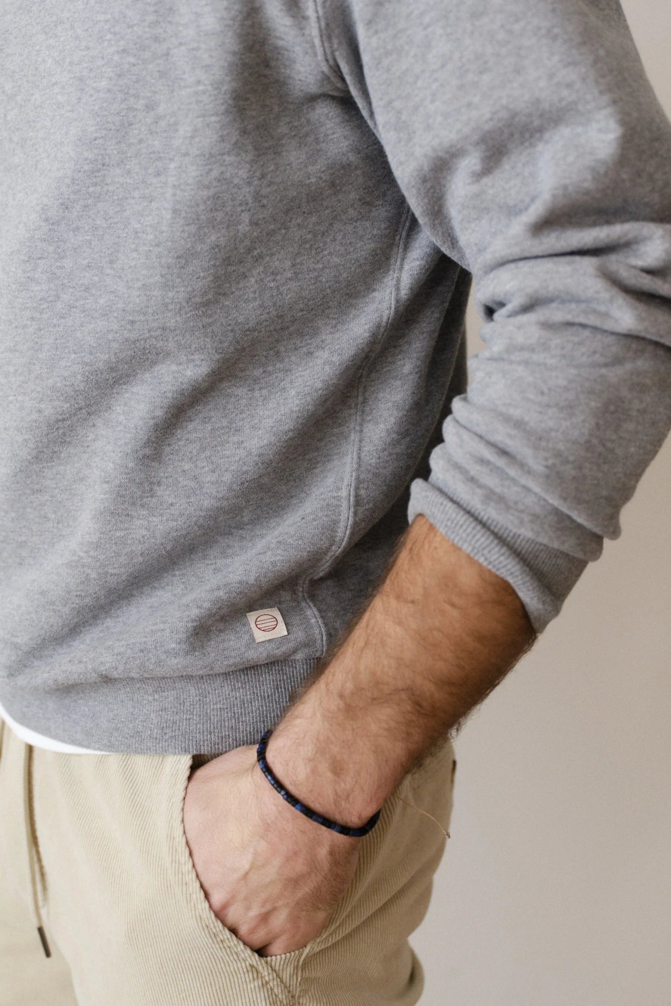 Person wearing a gray sweatshirt with a visible brand logo, standing against a plain background.