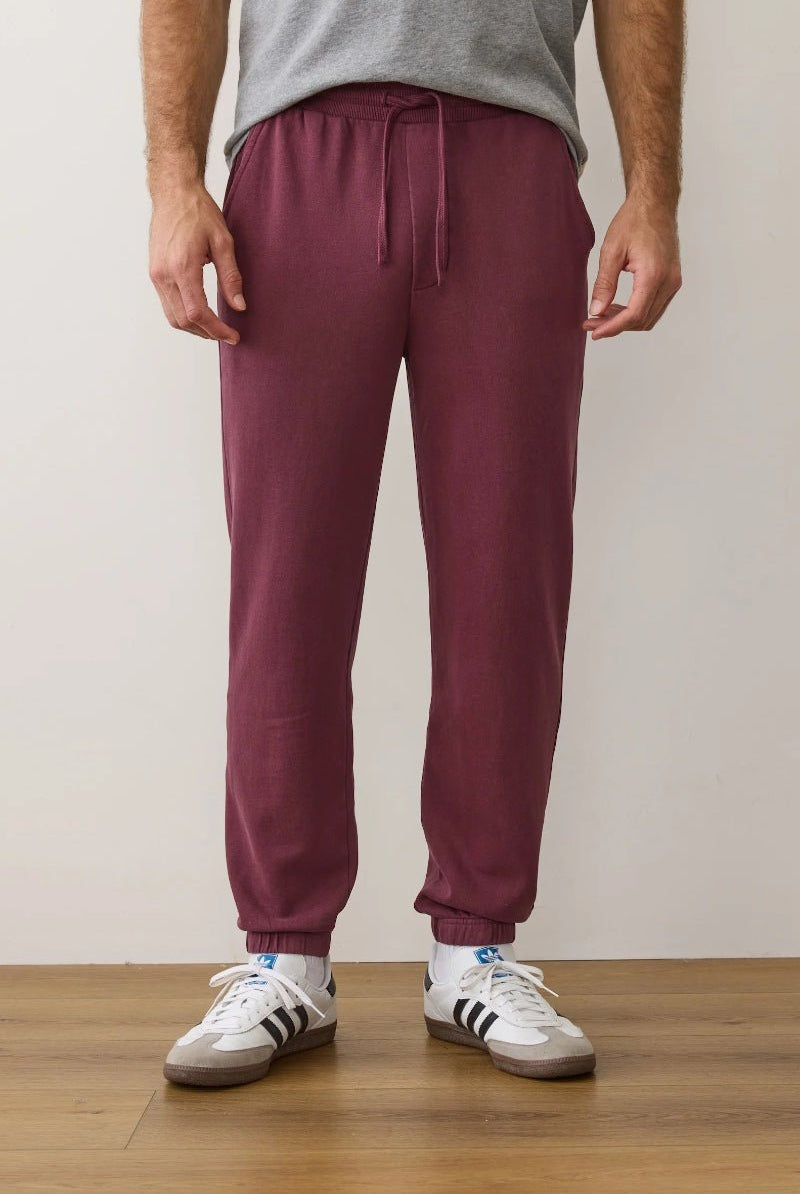 Person wearing maroon sweatpants and white sneakers on a plain background
