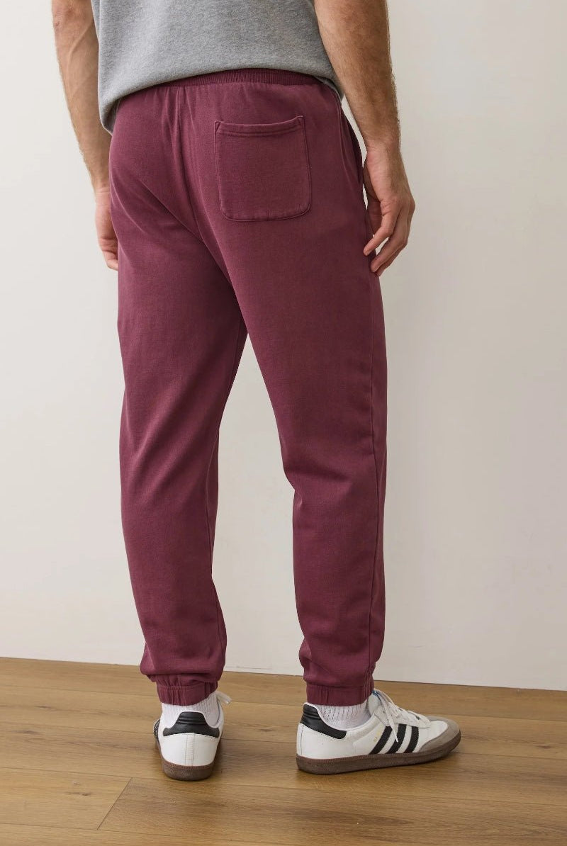 Person wearing maroon sweatpants and white sneakers on a wooden floor with a white wall background