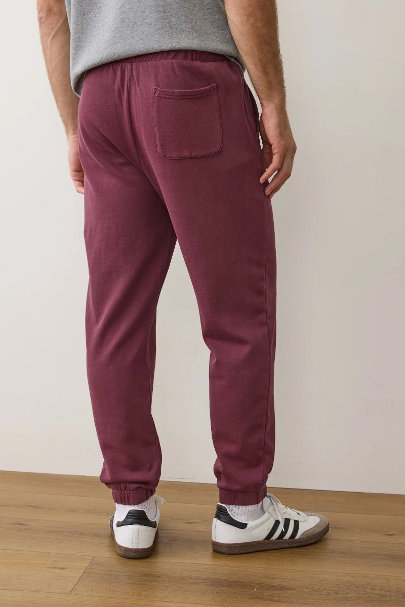 Person wearing maroon sweatpants and white sneakers on a wooden floor with a white wall background