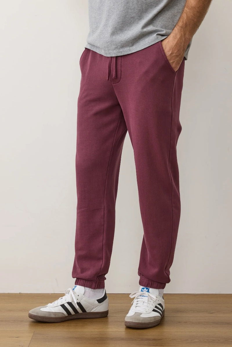 Person wearing maroon jogger pants and white sneakers with black stripes on a plain background