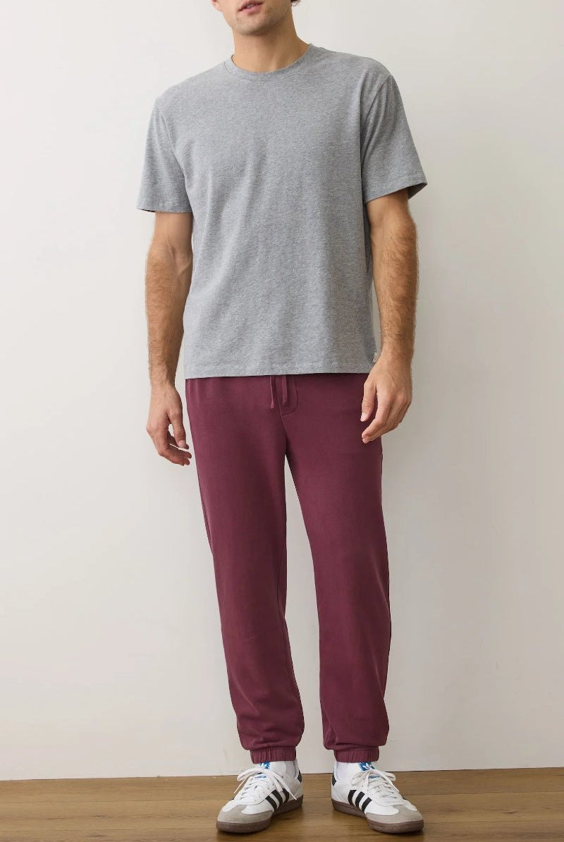 Person wearing a gray t-shirt and maroon pants with white sneakers on a plain background