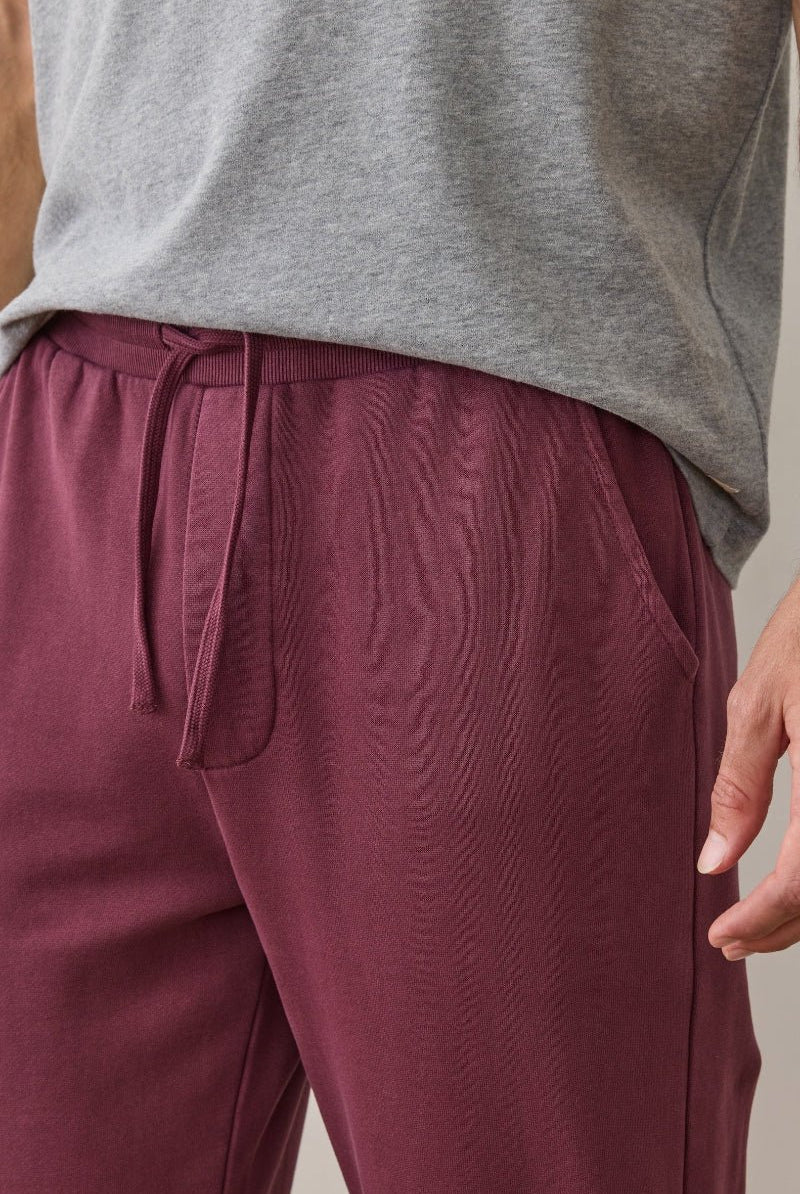 Person wearing maroon pants and a gray sleeveless shirt on a neutral background