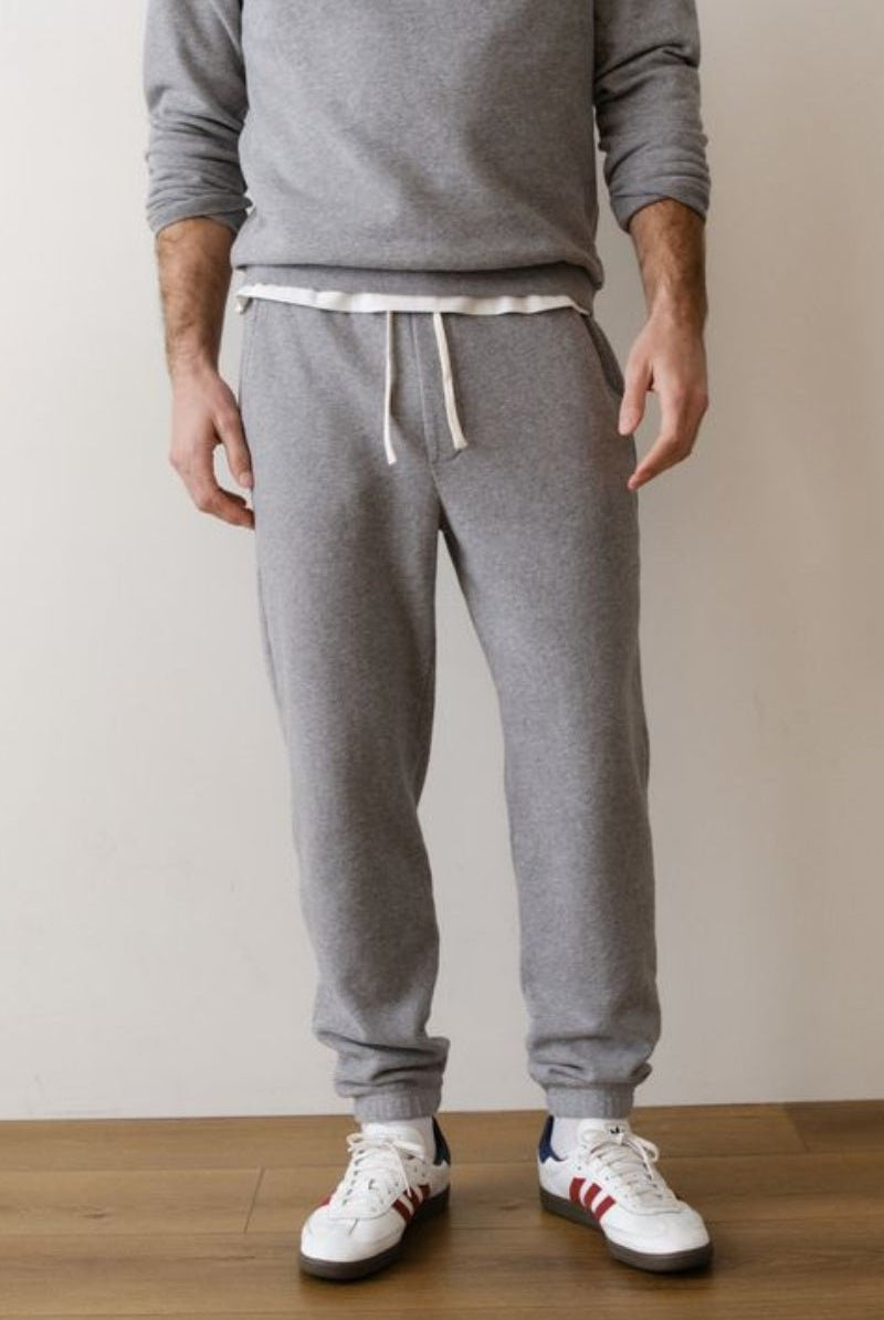 Person wearing gray sweatpants and white sneakers on a wooden floor with a beige wall background