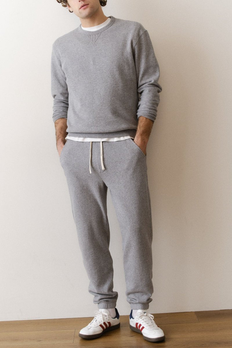 Person wearing a gray sweatshirt and pants with white sneakers against a plain background