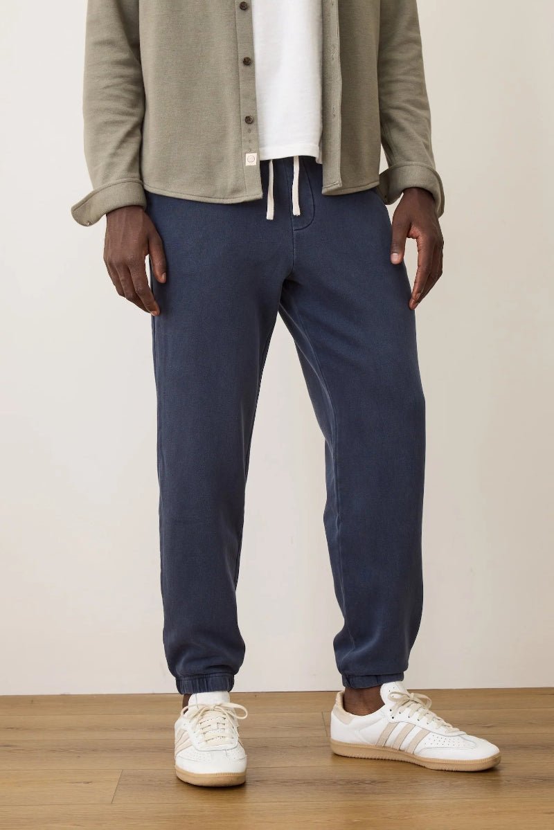 Person wearing navy jogger pants with a beige jacket and white sneakers on a plain background