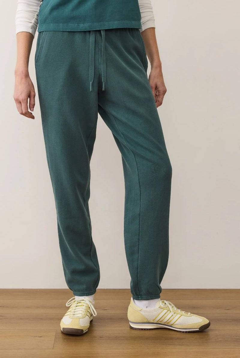 Person wearing teal jogger pants and yellow sneakers on a wooden floor.