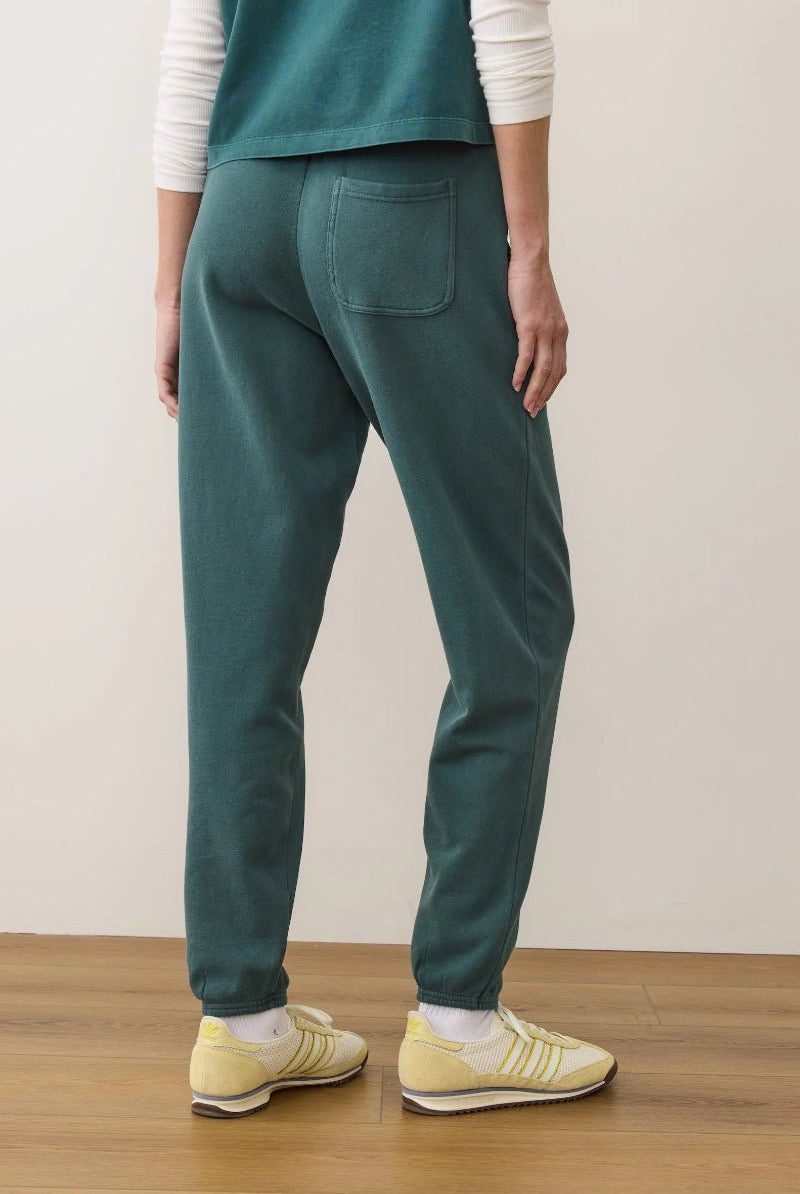 Person wearing teal pants and yellow shoes on a wooden floor with a white wall background