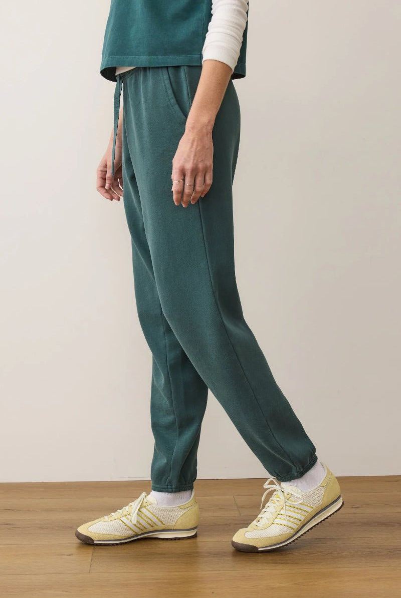 Person wearing teal pants and yellow sneakers on a wooden floor with a plain background