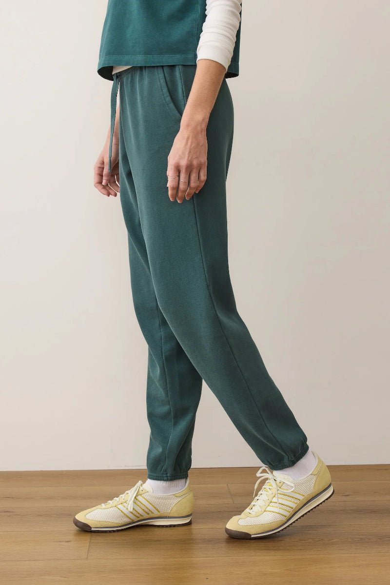 Person wearing teal pants and yellow sneakers on a wooden floor with a plain background