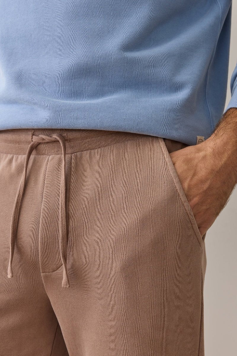 Person wearing a light blue sweater and brown pants with a neutral background