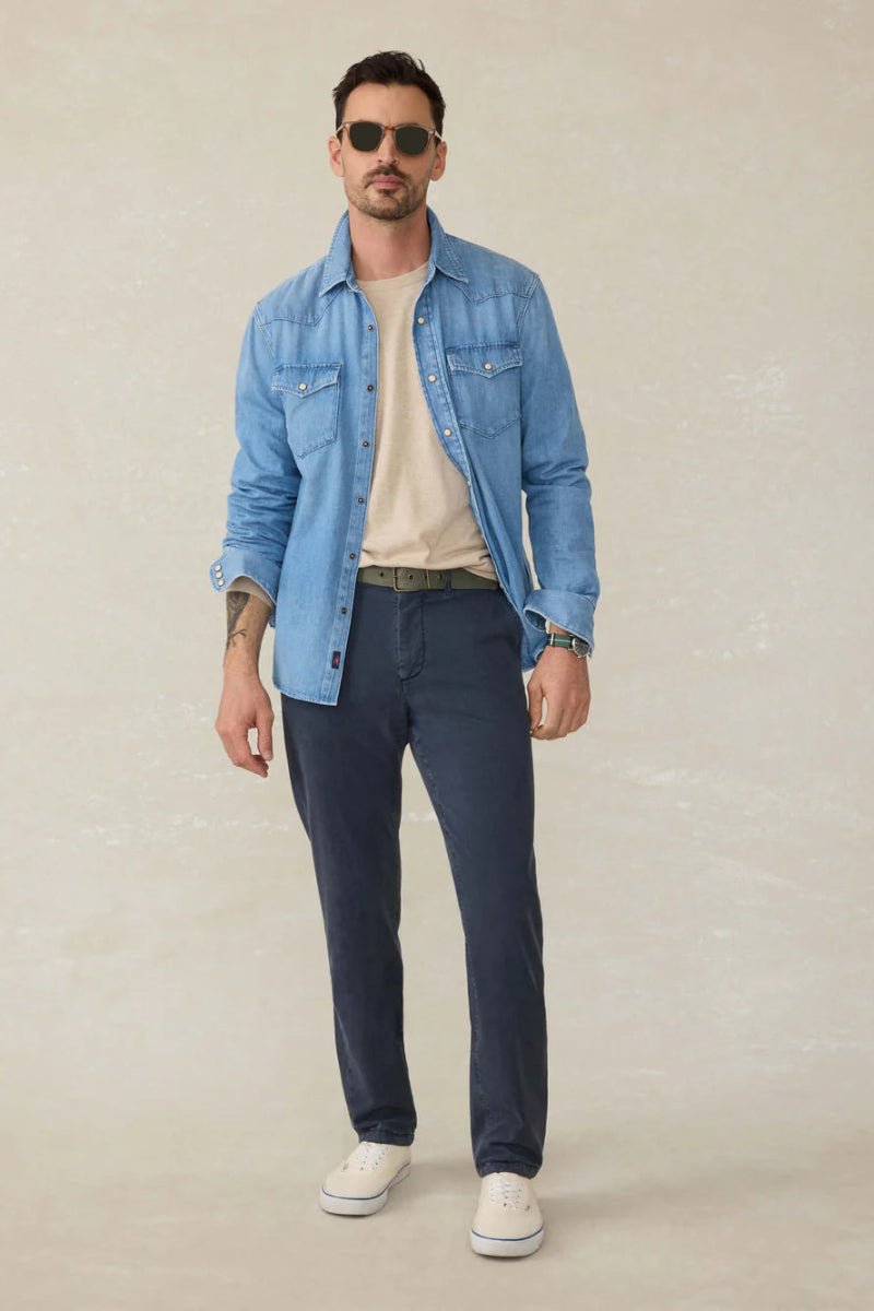 Man wearing a light blue denim jacket, white shirt, dark blue pants, and sunglasses on a beige background