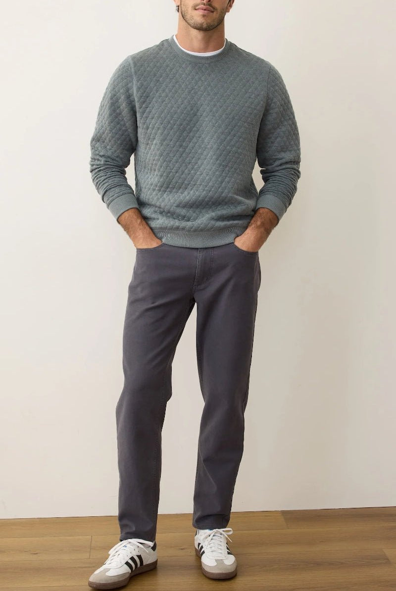 Man wearing a gray sweater and pants with white sneakers against a plain background