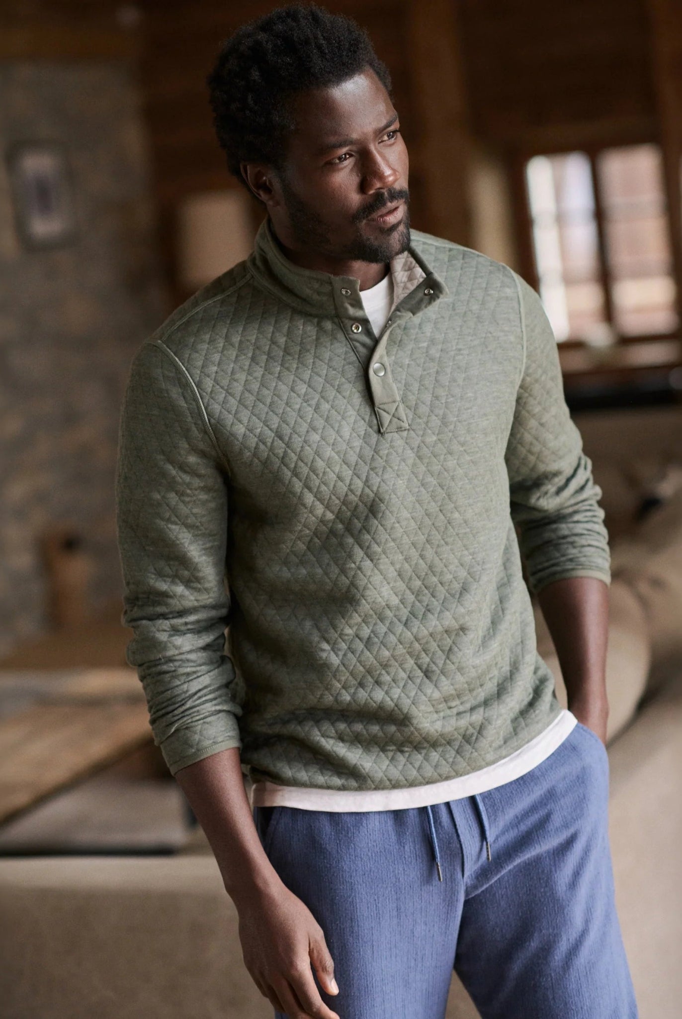 Man wearing a green quilted sweater and blue pants in a cozy indoor setting
