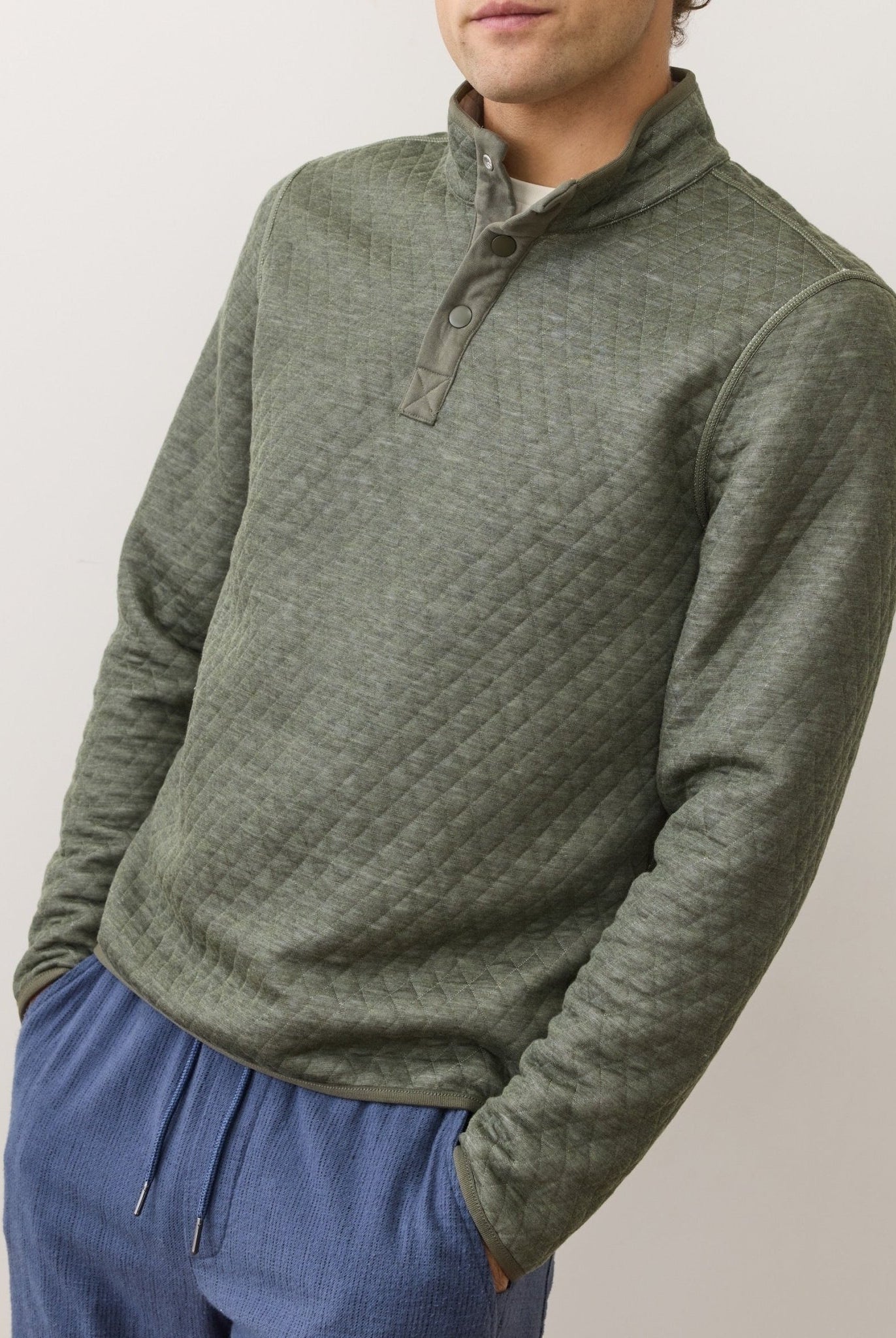Person wearing a green quilted pullover with a neutral background
