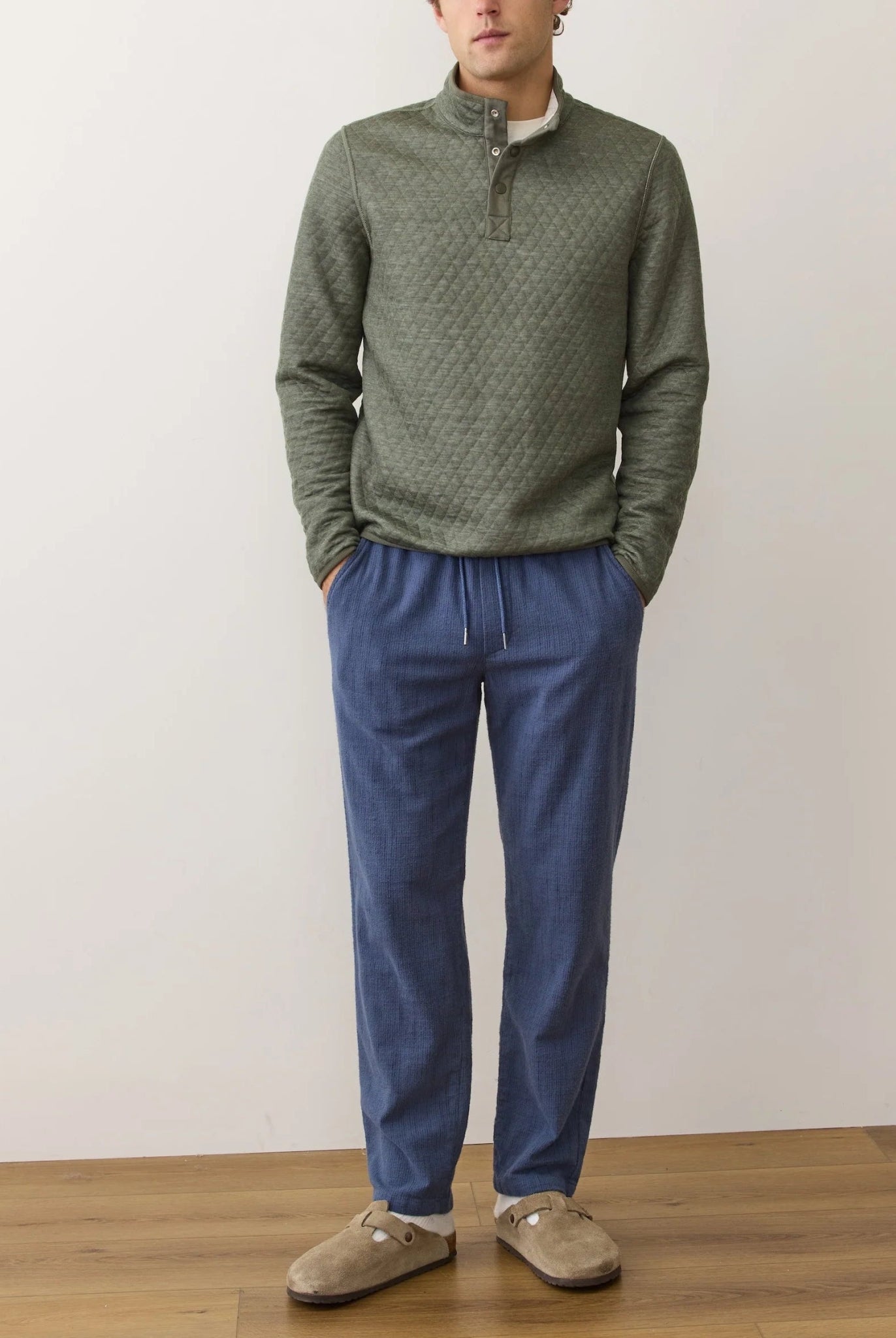 Man wearing a green patterned sweater and blue pants against a plain background